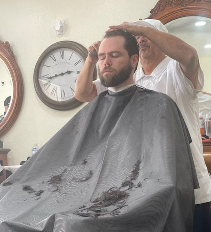 Oscar cutting a client's hair at the barbershop chair